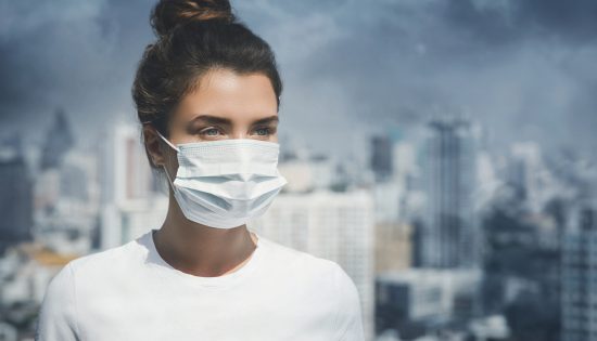 Young woman wearing face mask in polluted cityscape