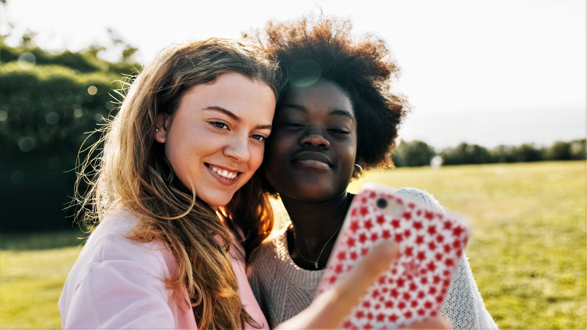 Photo of two girls taking a selfie in a field using a smartphone