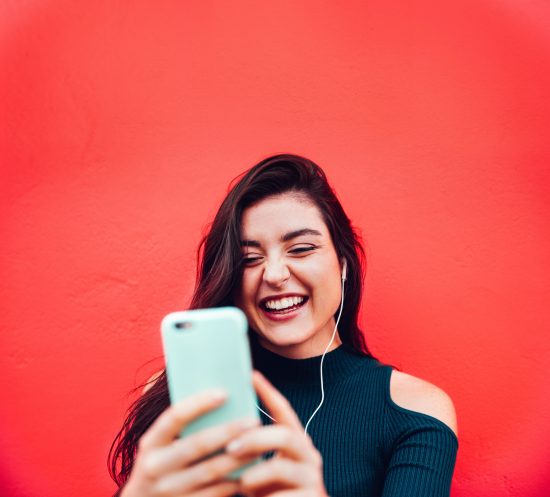 Young Woman Using Smart Phone Against Red Wall
