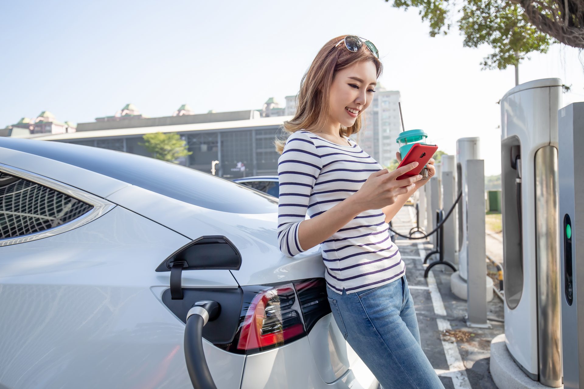 Young woman looking at smartphone while charging her electric car