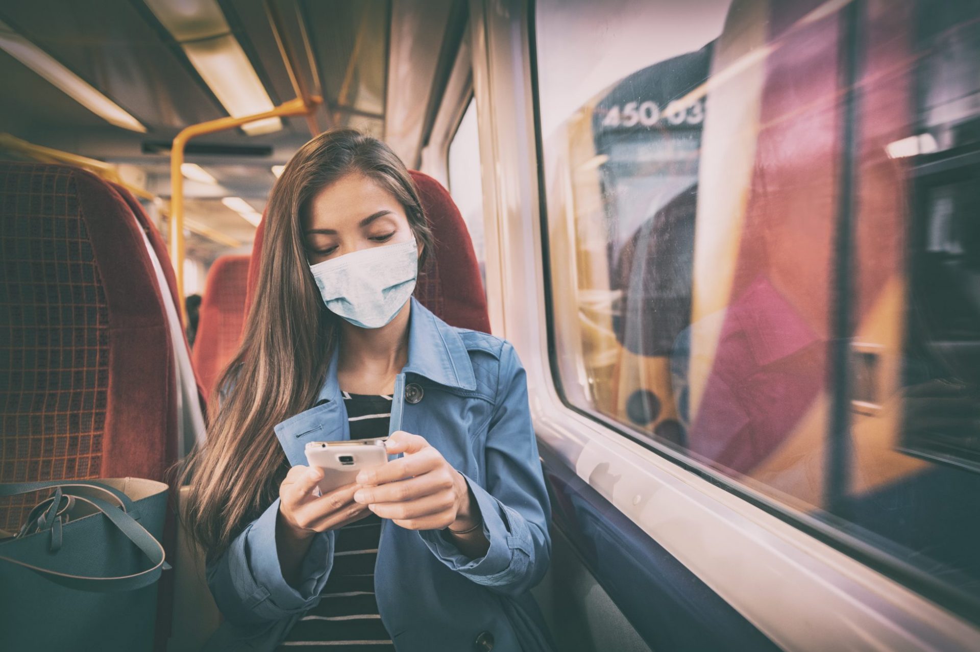 Young woman on train wearing mask and looking at smartphone