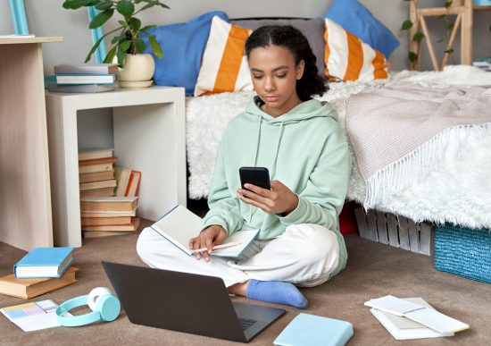 Teen girl working in bedroom on smartphone and laptop
