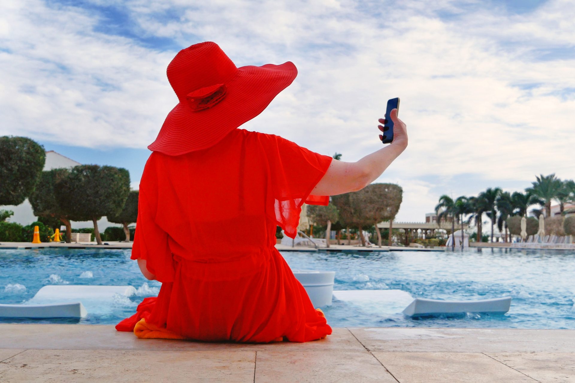 Woman in red next to pool taking selfie