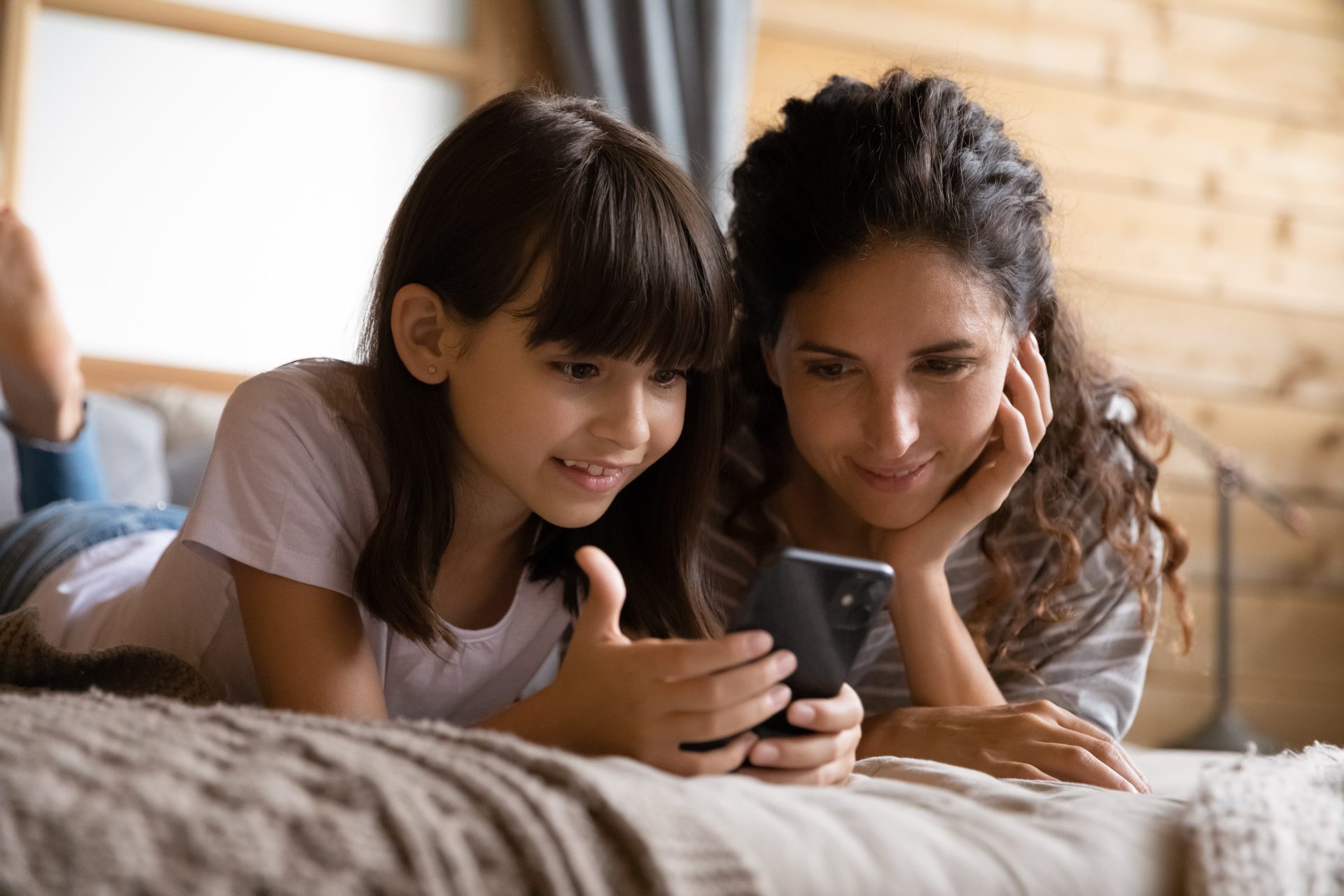 Mother and daughter on bed looking at smartphone